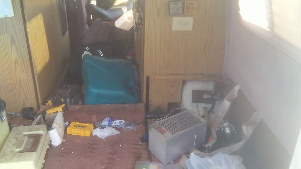 Interior of a cluttered RV with wood paneling and various items