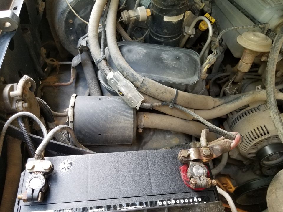 Engine bay showing battery terminals, alternator, and various hoses and wires