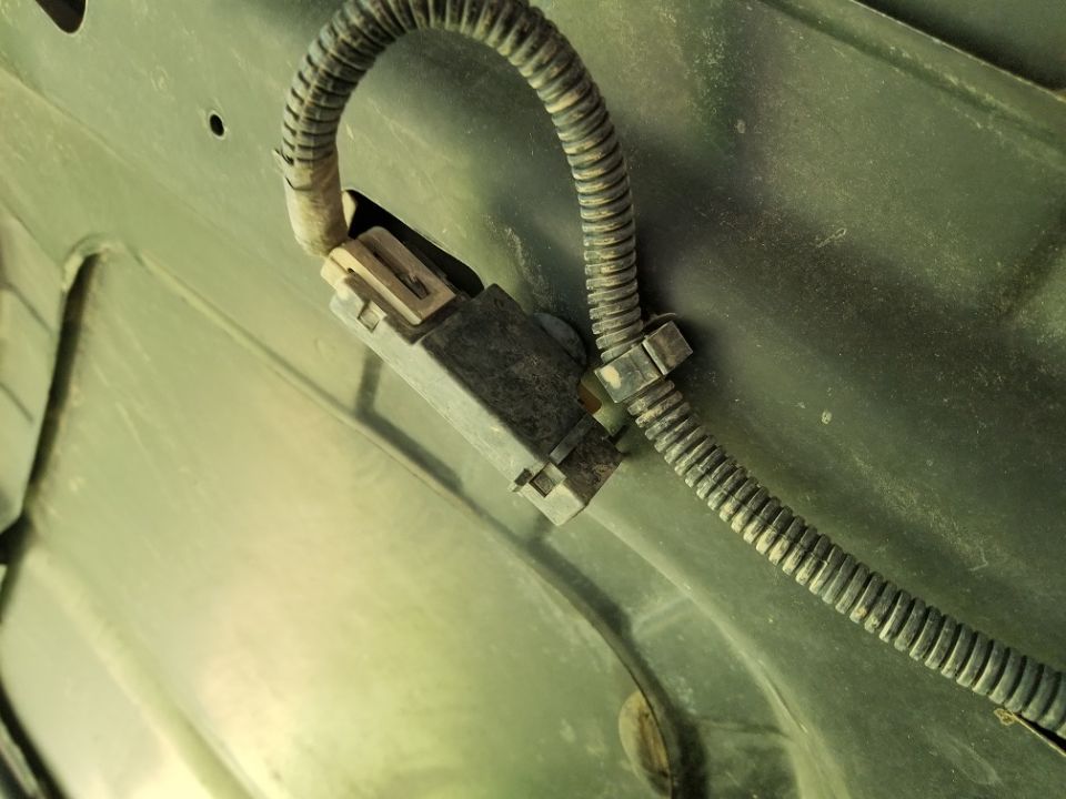 Close-up of a black electrical connector with a ribbed wire loom attached to a green metal surface