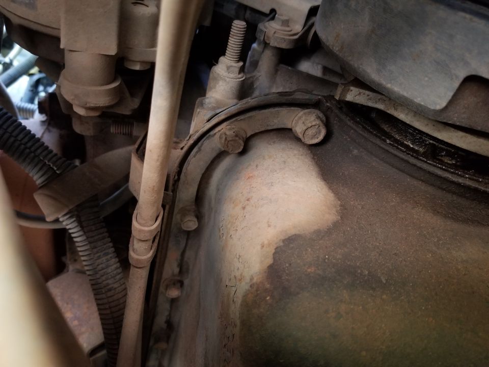 Close-up of engine oil pan and transmission housing with bolts and hoses visible