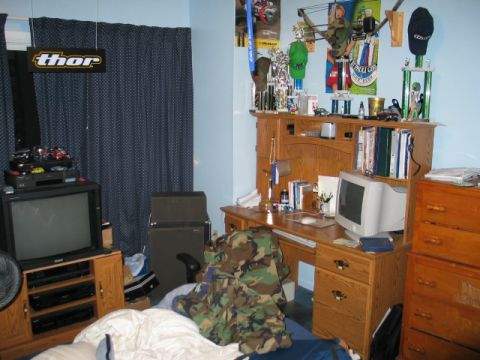 1995 Ford Bronco - A cluttered bedroom scene features a wooden desk with a computer and various items, alongside a television and trophies.