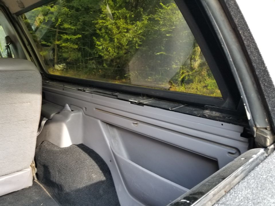 Interior rear cargo area of a vehicle, showing grey plastic trim, carpeted floor, and a portion of a seat