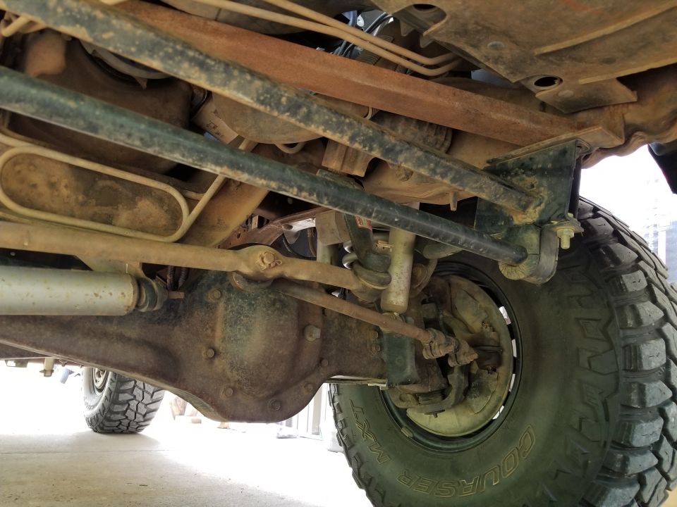 Undercarriage view of a 4x4 vehicle showing suspension, differential, and tire. Supermotors.net logo visible