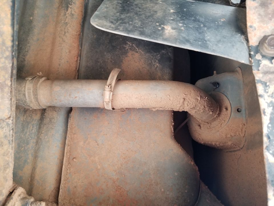 Undercarriage view of a rusty exhaust pipe with hose clamps, showing dirt and grime