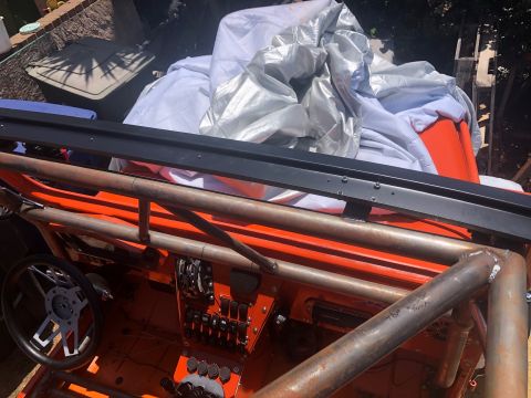 1992 Jeep Wrangler - Interior view of an orange off-road vehicle, a custom roll cage, aftermarket steering wheel, and dashboard switches.