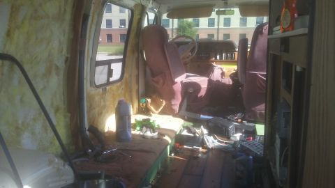 1988 Dodge RV/Conversion Chassis - Cluttered interior of a van, showing seats and unfinished walls. Building visible outside.