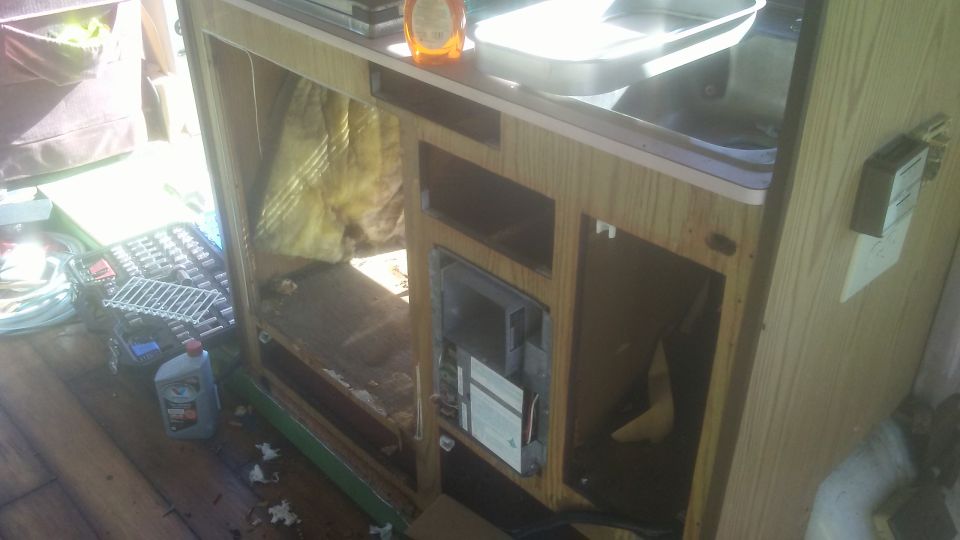 RV interior with cabinets removed, tools and a bottle of fluid on the floor