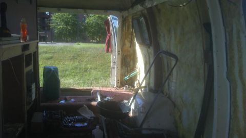 1988 Dodge RV/Conversion Chassis - The interior of a van shows signs of extensive modification and disrepair, with the rear door open to an outdoor scene.