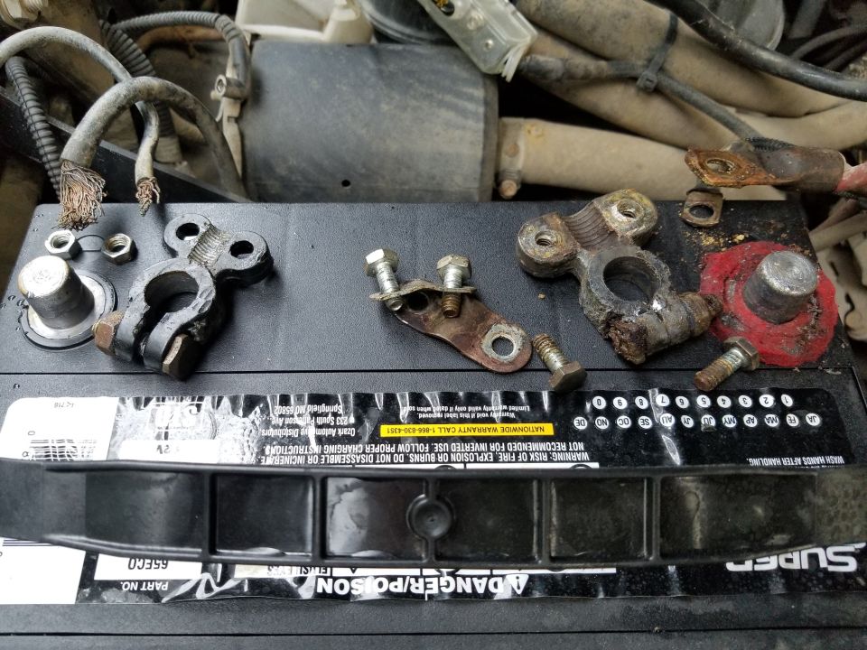 Corroded battery terminals and bolts laid out on a car battery