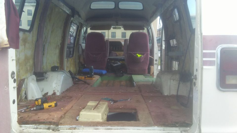 Interior of a dismantled van, showing bare walls, floor, and two maroon seats
