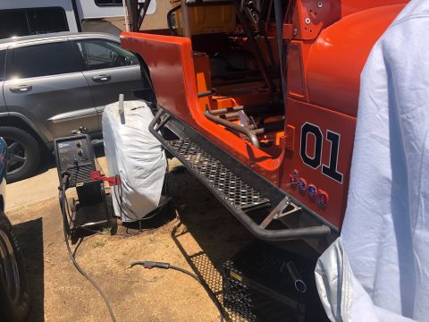 1992 Jeep Wrangler - Orange Jeep with "01" decal and roll cage, seen next to a silver SUV and welding equipment.