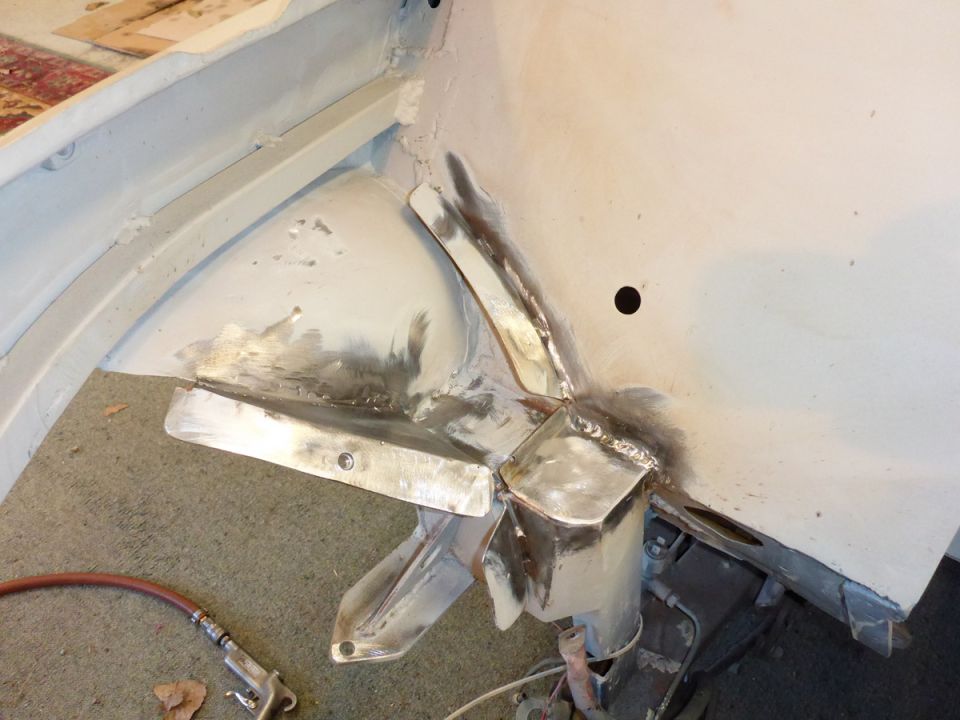 Car body being repaired with new metal welded in place. Air tool and hose visible on the floor