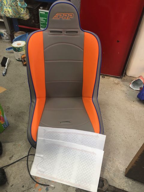 1992 Jeep Wrangler - Gray and orange PRP off-road suspension seat resting on a garage floor with a diamond-plate panel leaning in front.