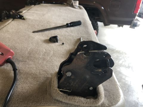1980 Ford Bronco - Close-up of a car seat latch mechanism, with tools nearby. A dark SUV is visible in the background.