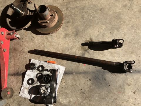 1978 Ford Bronco - Various automotive parts, including a driveshaft and hub components, are spread out on a garage floor.