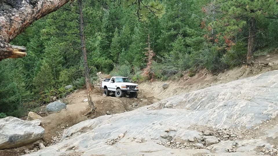 White pickup truck driving up a steep, rocky trail in a forest