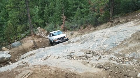 1995 Ford Bronco - White Ford F-150 truck carefully maneuvers over a challenging rocky terrain on an off-road trail.