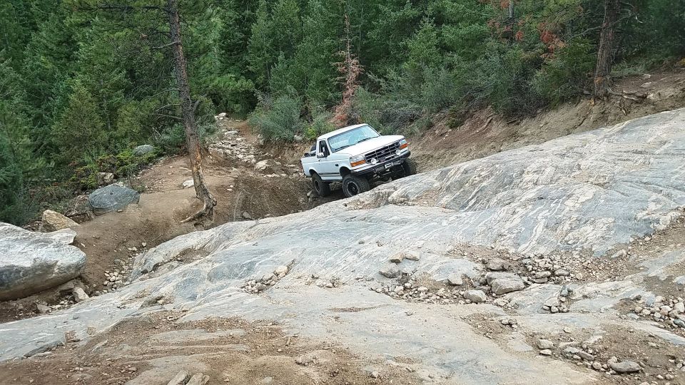 1995 Ford Bronco climbing a steep, rocky trail with trees in the background