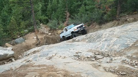 1995 Ford Bronco - A white pickup truck navigates a steep, rocky incline on an off-road trail.