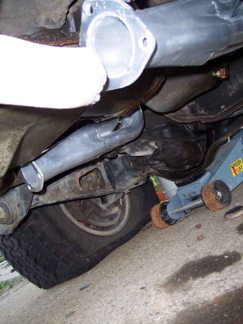 1990 Ford Bronco - Underside view of a truck exhaust system mid-install, showing a new bare-metal Y-pipe with a three-bolt flange and slip-fit connections rou…