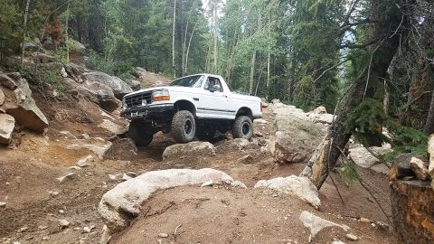 1995 Ford Bronco - White 1995 Ford Bronco tackling a challenging rocky trail in a wooded area.