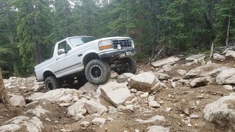 1995 Ford Bronco - A white Ford Bronco tackles a challenging rocky trail in a wooded area.