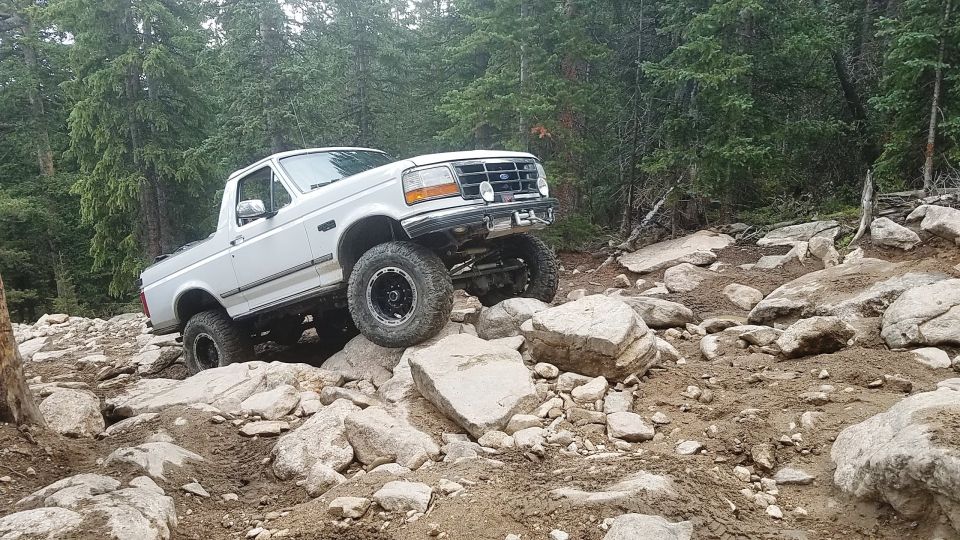 White Ford Bronco with lifted suspension navigating a boulder-strewn mountain path