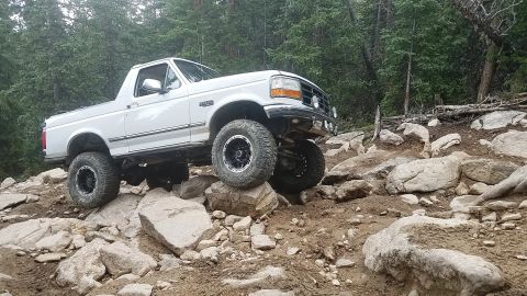 1995 Ford Bronco - White 1995 Ford Bronco tackles a challenging rocky trail, demonstrating its off-road capabilities.