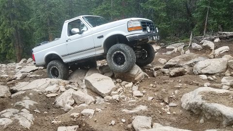 1995 Ford Bronco - White 1995 Ford Bronco tackling a challenging off-road course with large rocks.