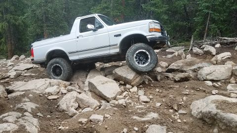 1995 Ford Bronco - White Ford Bronco traverses a challenging rocky terrain with one wheel lifted.