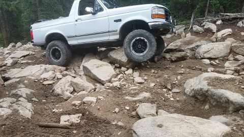 1995 Ford Bronco - White 1995 Ford Bronco tackles a challenging rocky trail, demonstrating its off-road capabilities.