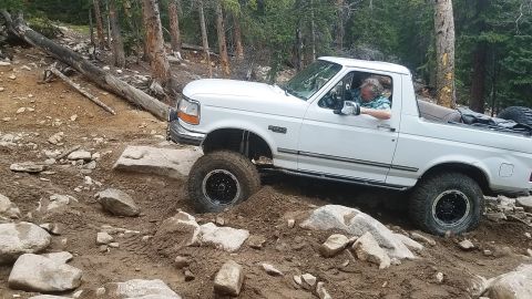 1995 Ford Bronco - White Ford Bronco tackling a challenging off-road course in a wooded area.