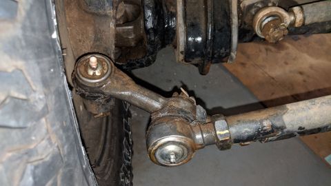 1995 Ford Bronco - This close-up photo shows the rusty tie rod ends and steering linkage of a 1995 Ford Bronco. The vehicle's tire is visible on the left side…
