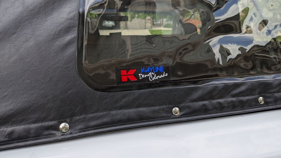 Close-up of a black soft top window with a Kayline logo and metal snaps.