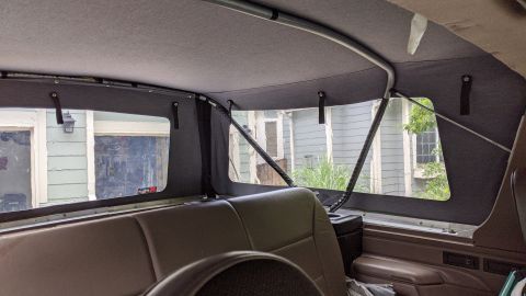 1995 Ford Bronco - Interior view of a vehicle's soft top, showing the fabric lining, metal support bars, and rear windows looking out onto a house.