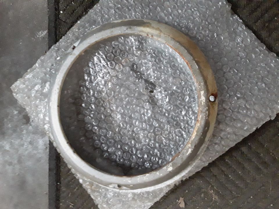 Round metallic part with chipped white paint and rust, on bubble wrap.