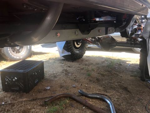 1992 Jeep Wrangler - The underside of a vehicle shows a large exhaust pipe curving upwards, a differential, and suspension components. A black plastic milk crat…