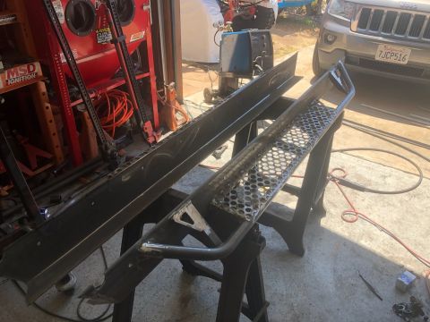 1992 Jeep Wrangler - Two custom metal fabricated parts, possibly rock sliders or bumpers, are displayed on sawhorses in an outdoor workshop setting. A Jeep Wran…