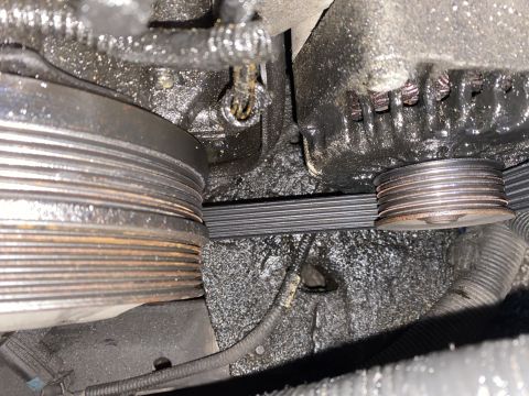 Close-up of oily serpentine belt and pulleys on a car engine.