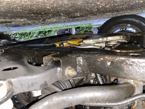 Underside view of vehicle frame and leaf spring, oily components, roadside