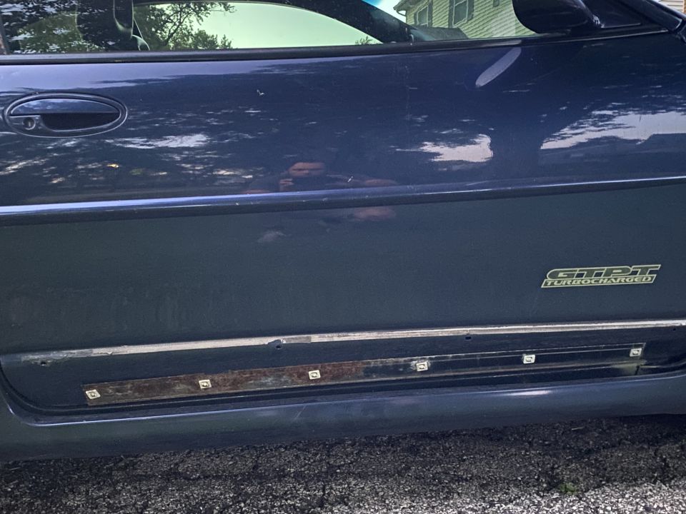 Dark blue sedan side panel with GTPT TURBOCHARGED emblem and rusted rocker trim.