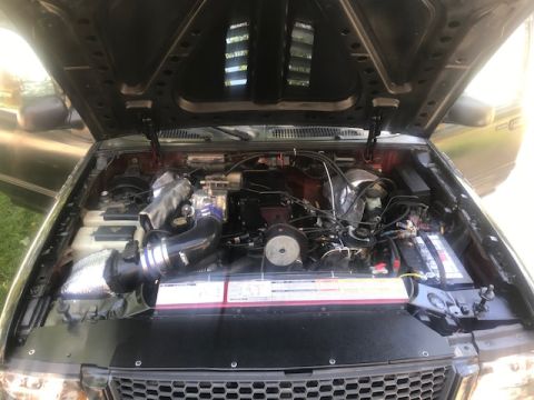 2000 Ford Explorer - The open hood of a dark red Ford Explorer reveals a modified engine bay with a custom intake system and various engine components. The vehi…
