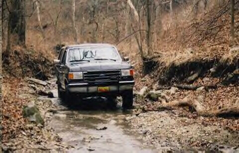 1989 Ford Bronco - A 1989 Ford Bronco navigates a muddy, wooded trail.