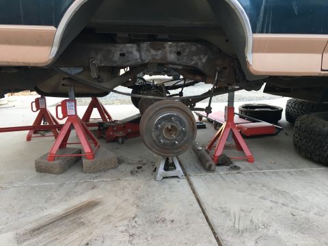 1995 Ford Bronco - The underside of a dark green and tan 1995 Ford Bronco is shown supported by jack stands and a floor jack. The rear drum brake assembly is…