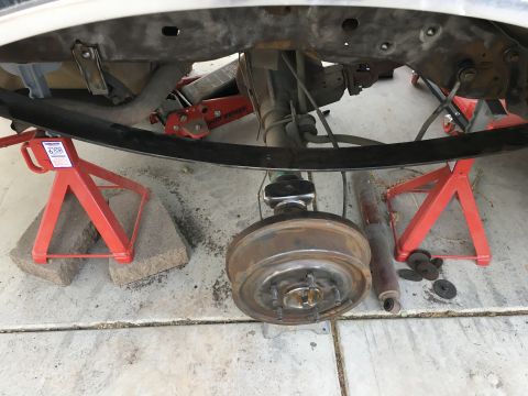 1995 Ford Bronco - The underside of a vehicle is shown, supported by red jack stands. A drum brake assembly and a shock absorber are visible, along with parts…