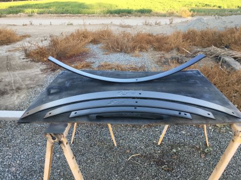1995 Ford Bronco - Several leaf springs are laid out on a black surface atop sawhorses, with a grassy field and dirt road in the background.