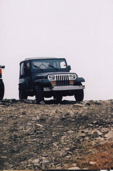1979 Ford F-150 - A dark Jeep Wrangler is parked on a rocky incline, with another vehicle partially visible to the left.