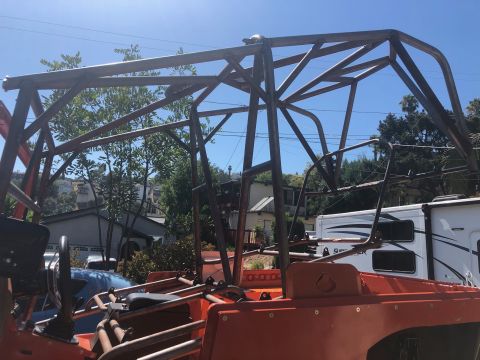 1992 Jeep Wrangler - A custom-built roll cage is installed over the interior of an orange vehicle, with a trailer visible in the background.
