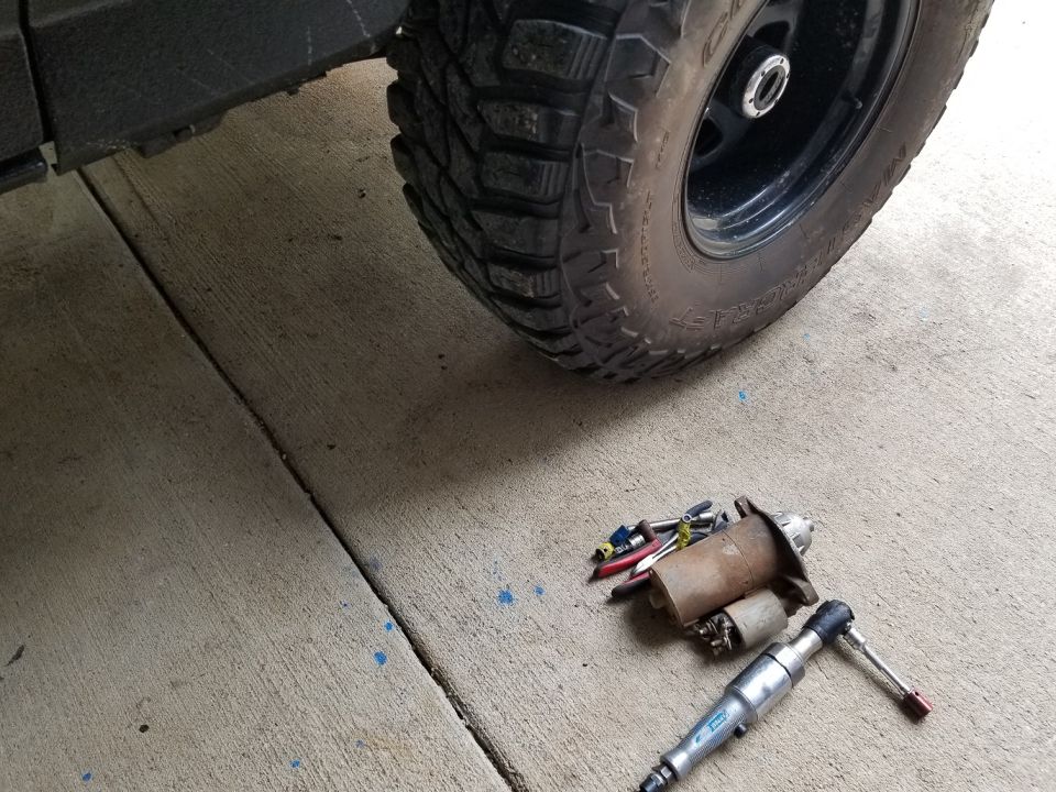 starter motor, pliers, and socket wrench on concrete near a tire
