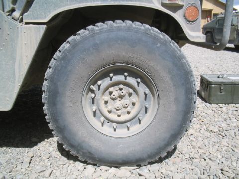 1981 Ford Bronco - A Humvee's large wheel and tire are shown, with another military vehicle in the background.
